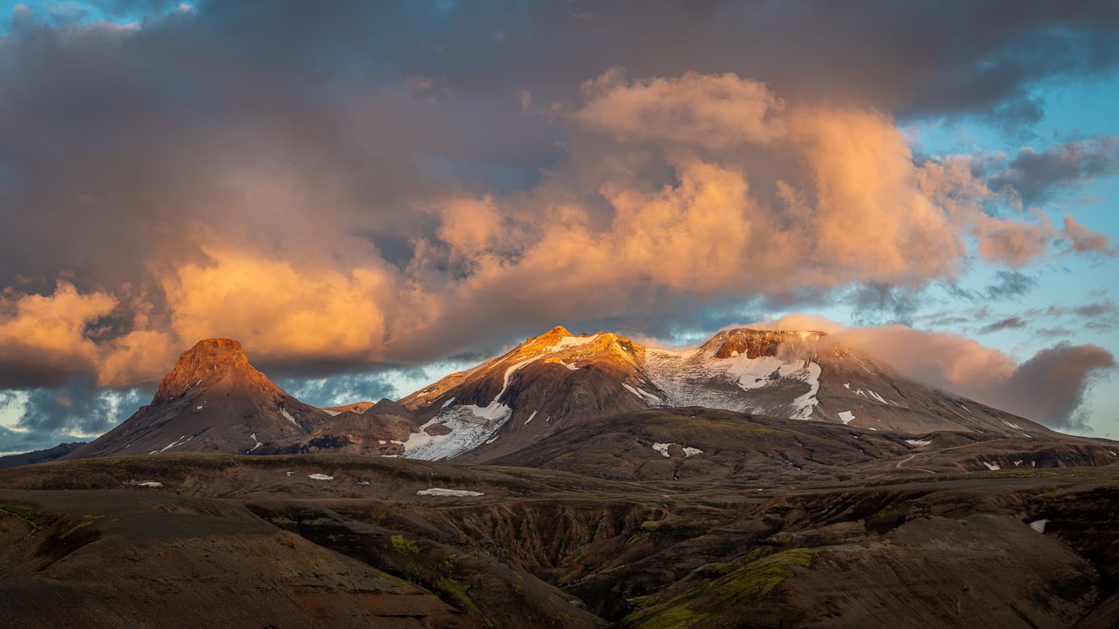 Orange dawn light illuminating snow-streaked mountains and clouds in the Icelandic highlands
