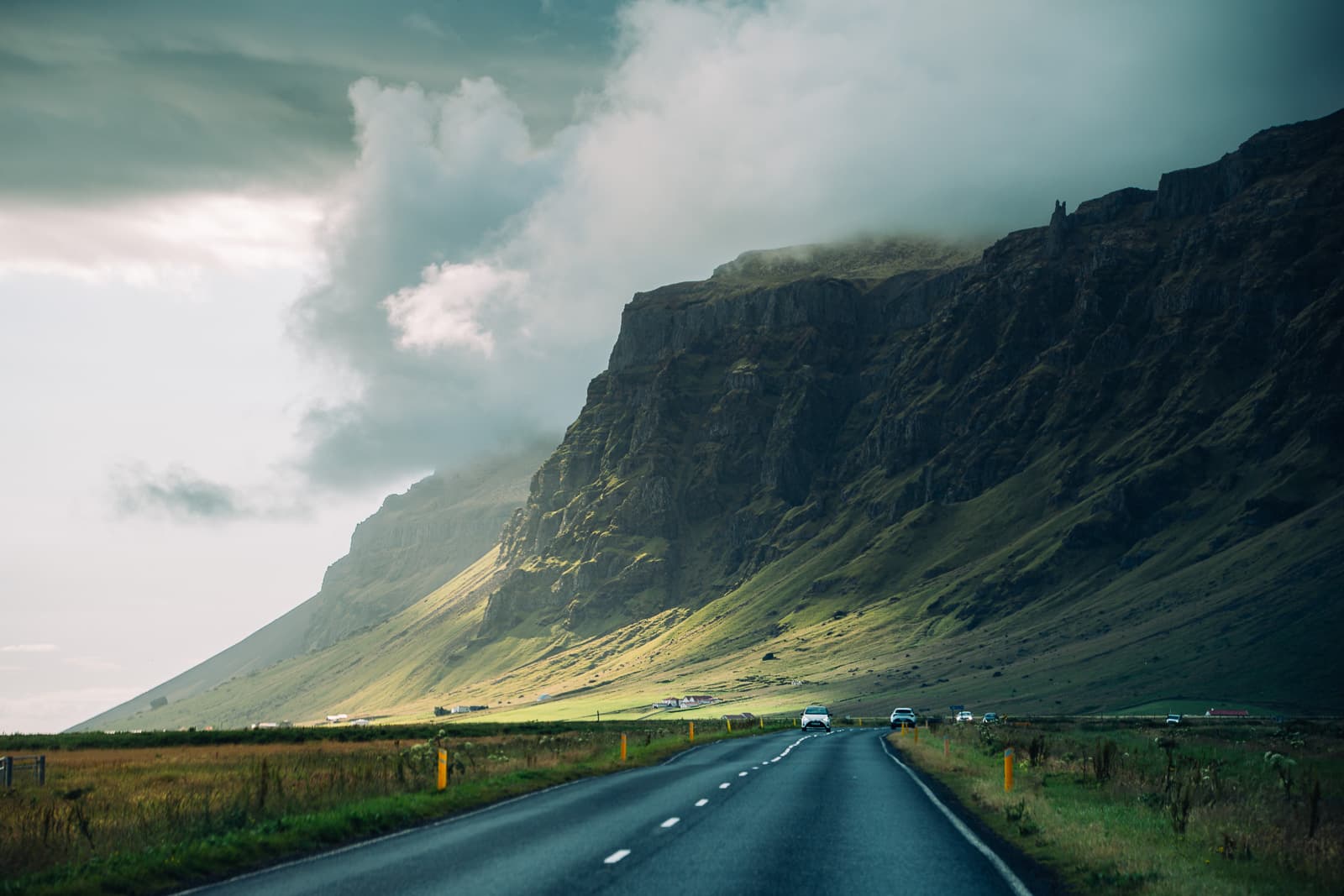 A paved road beneath steep green cliffs and low clouds in Iceland