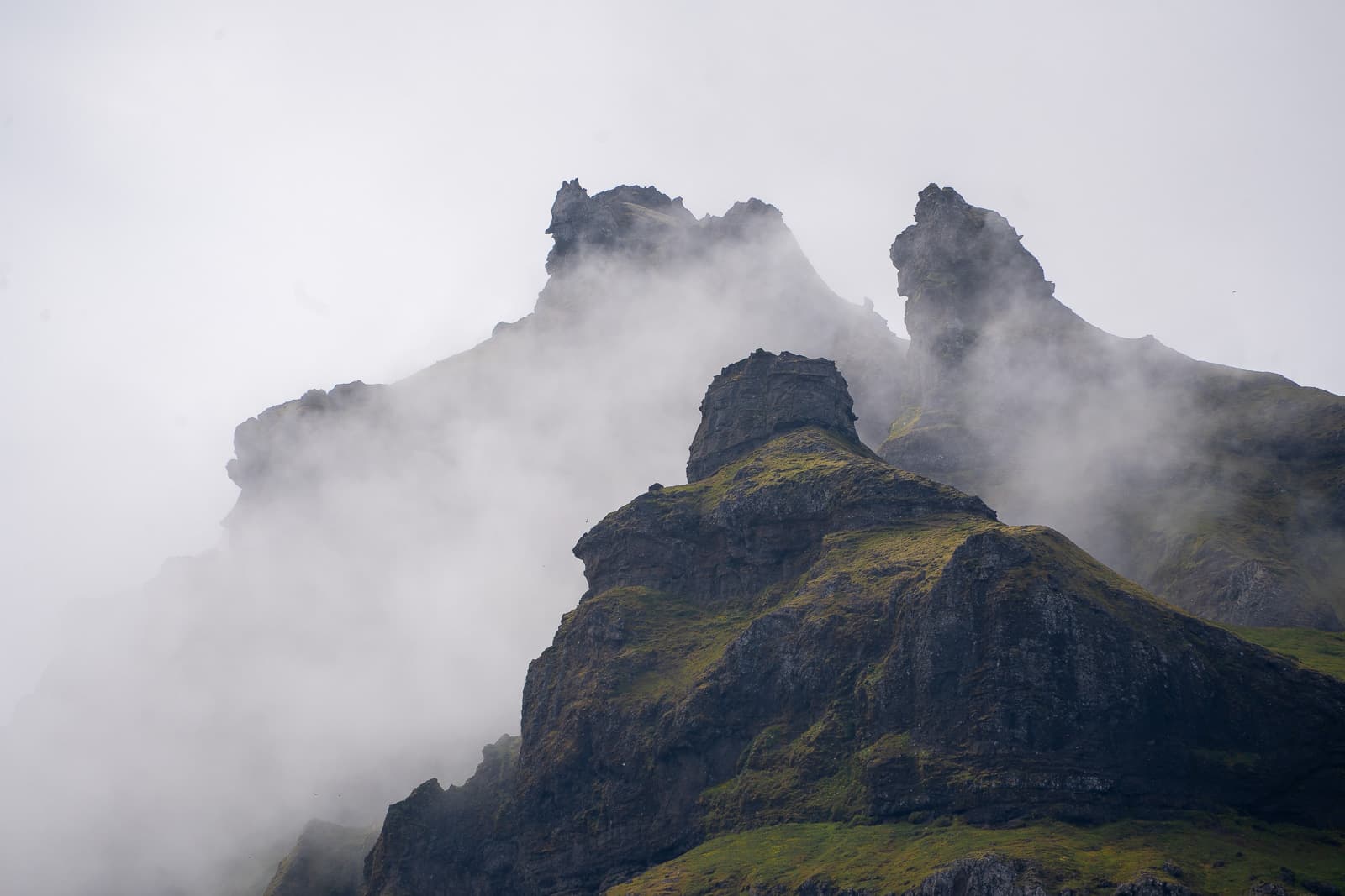 Jagged rock pinnacles with green moss emerging through mist in Iceland