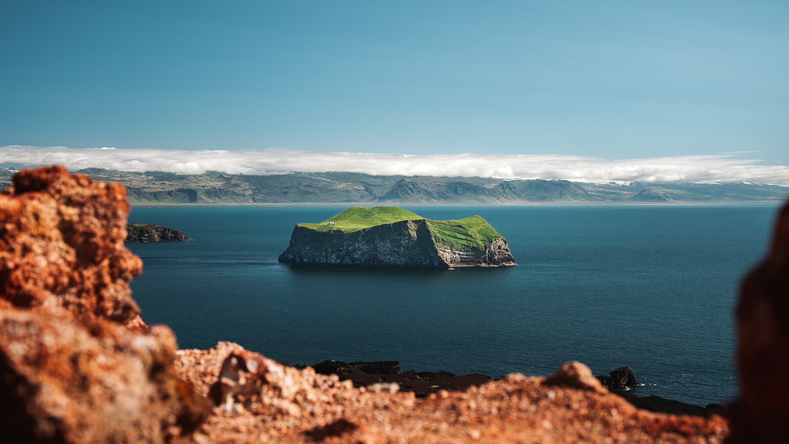 A green island in the blue Atlantic, framed by red volcanic cliffs in the Westman Islands, Iceland
